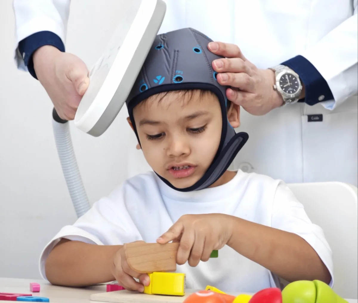 คุณหมอวางเครื่องกระตุ้นสมอง TMS ให้เด็ก ขณะเด็กเล่นของเล่นฝึกทักษะ ที่ InterRehab NeuroBridge